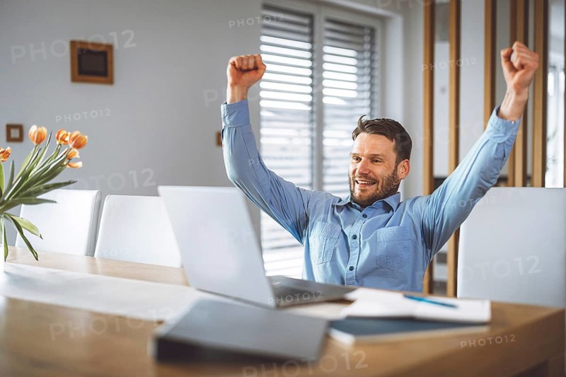 Excited caucasian man cheering for his team, watching a football game on his laptop, man celebrating a win with clenched fists