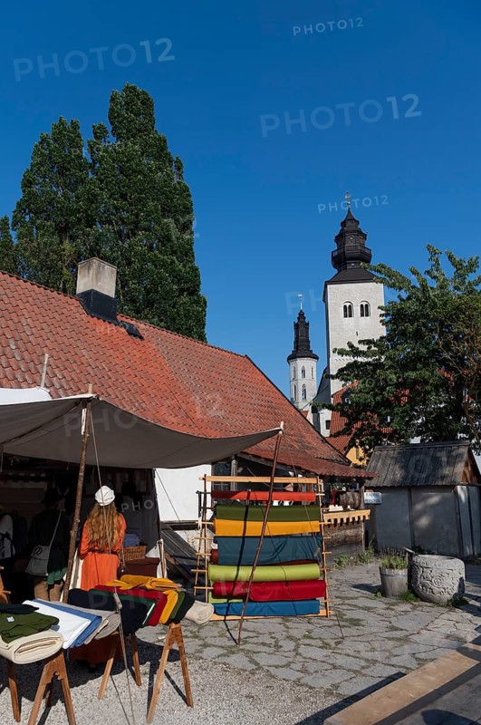 Stand with colourful bales of fabric and woman in medieval traditional costume, in the background St. Mary's Church or Visby Cathedral, Medieval Week, Hanseatic City of Visby, UNESCO World Heritage Site, Gotland Island, Sweden, Europe