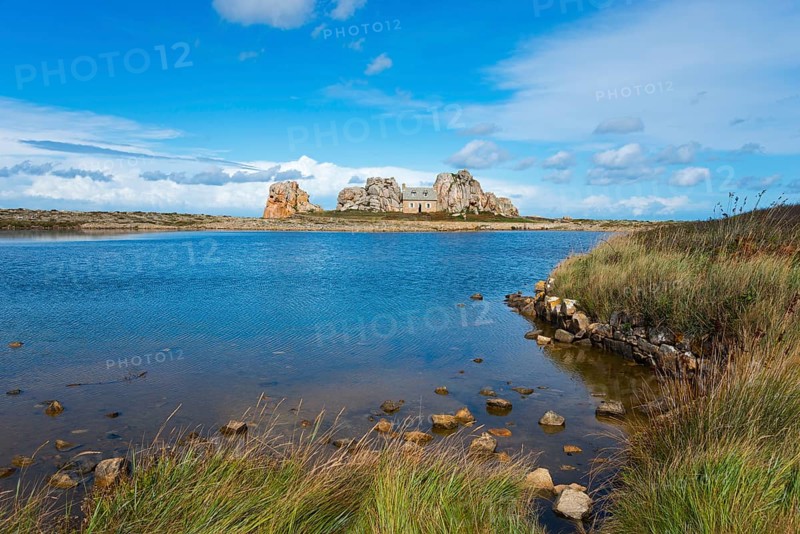 A house stands between rocks on a lake under a blue sky with clouds, House between the rocks on the granite coast, Le Gouffre, Plougrescant, Côtes-d'Armor, English Channel, Brittany, France, Europe