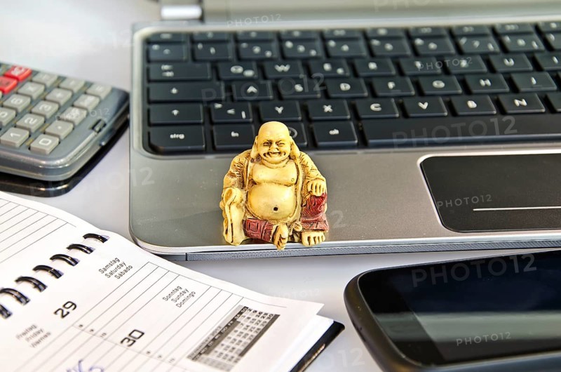 Buddha statue sitting on a laptop in front of office equipment