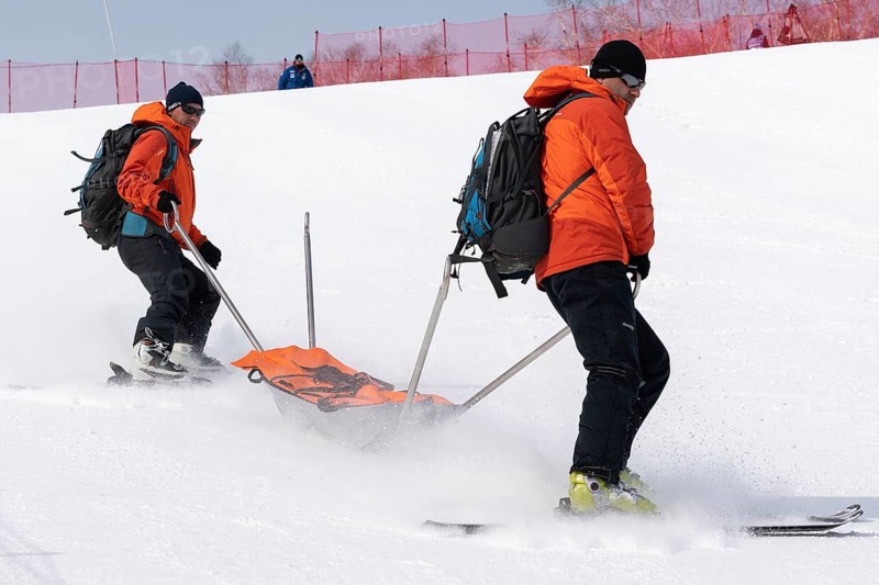 KAMCHATKA, RUSSIA, MARCH 28, 2019: Rescuers Kamchatka Rescue Squad on alpine ski with stretcher skiing down mount slope for first medical aid, evacuation injured sportsman during competition alpine skiing