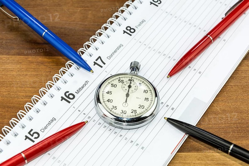 Pens lying on schedule and pointing towards stopwatch (with captions of the days of the week in German)
