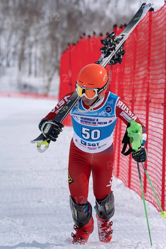 MOROZNAYA MOUNT, KAMCHATKA PENINSULA, RUSSIA, MARCH 28, 2019: Russian Alpine Skiing Cup, slalom. Mountain skier Shishkin Vitaliy Altai Region climbs on foot along ski slope with skis on shoulder
