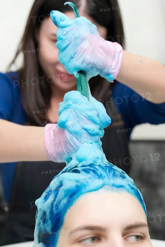 Hairstylist washes female head with dark blue hair color after hair dyeing process in beauty salon. Professional in pink protective gloves washing long hair with shampoo