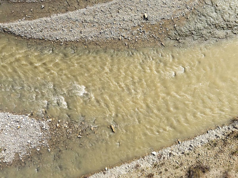 Muddy water flowing in the arda river near mignano val tolla in piacenza, italy, creating small waves and rapids on a sunny day