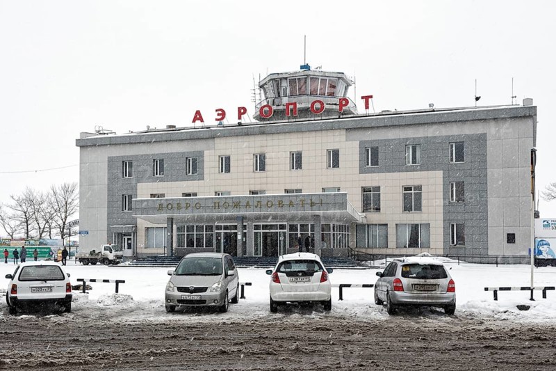 PETROPAVLOVSK, KAMCHATKA PENINSULA, RUSSIA, MAR 19, 2015: Winter view of building of commercial airport terminal Petropavlovsk-Kamchatsky and cars on station square, during snowfall, poor visibility