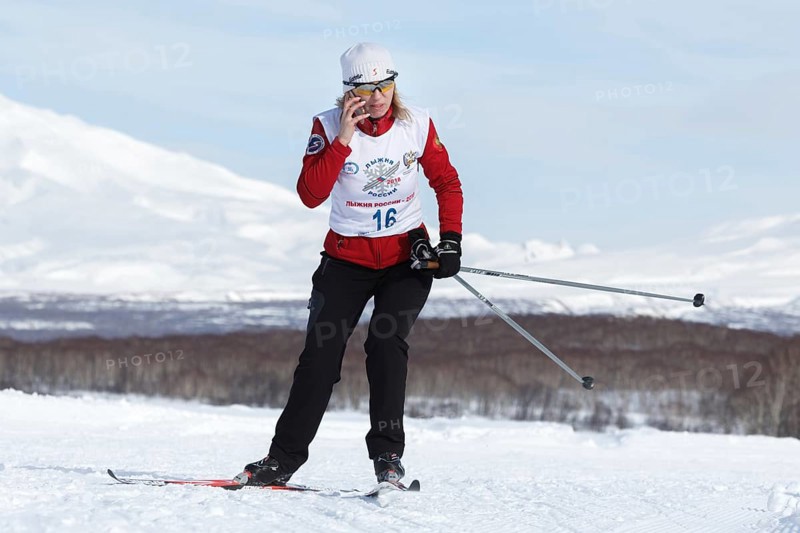PETROPAVLOVSK CITY, KAMCHATKA PENINSULA, RUSSIAN FAR EAST, FEB 10, 2018: Sportswoman skier running along the winter ski track and talking on smartphone. All-Russia mass ski race, Ski Track of Russia