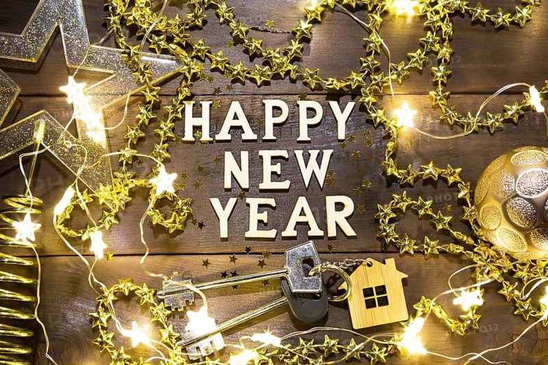 House key with keychain cottage on a festive background with sequins, stars, lights of garlands. Happy New Year-wooden letters, greetings, greeting card. Purchase, construction, relocation, mortgage