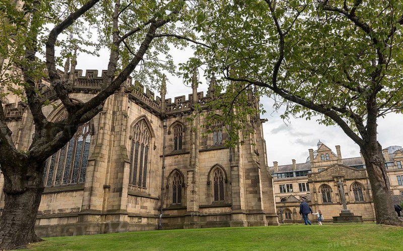 Manchester, United Kingdom, September 24 2016: Exterior view of the famous medieval building of the cathedral of the city of Manchester in United Kingdom with people walking in the gardens, Europe