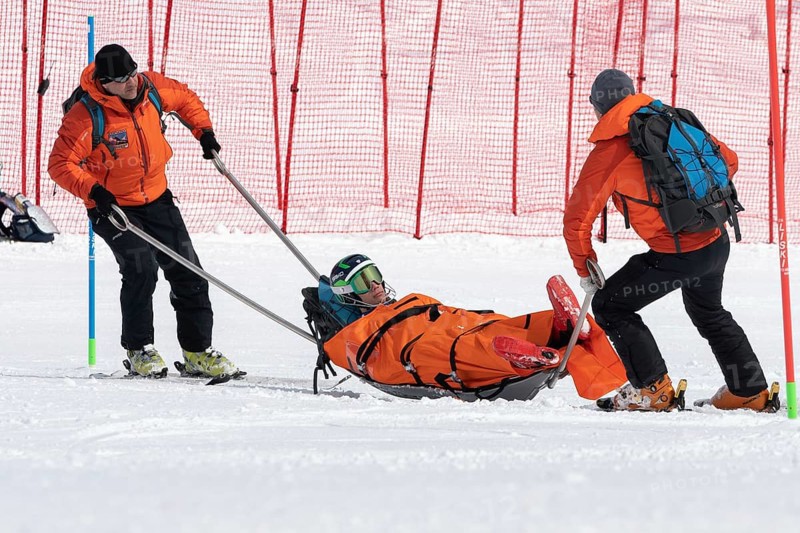 KAMCHATKA PENINSULA, RUSSIA, MAR 28, 2019: Rescuers Kamchatka Rescue Squad on alpine ski evacuate injured skier sportsman from mountain on tactical rescue stretchers during competition alpine skiing