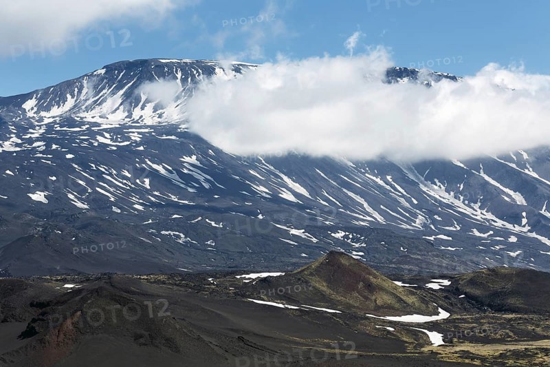 Volcanic landscape of Kamchatka Peninsula: beautiful summer view of cone of active Plosky Tolbachik Volcano and clouds partially hiding the top of volcano. Eurasia, Russian Far East, Kamchatsky Region, Klyuchevskaya Group of Volcanoes