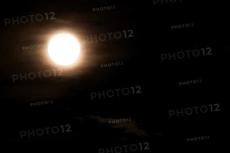 Super bright full moon and partially covered with dramatic black sky clouds
