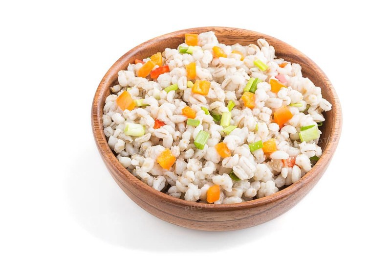 Pearl barley porridge with vegetables in wooden bowl isolated on white background. Side view, close up. Russian traditional cuisine