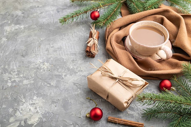 Christmas or New Year composition. Decorations, box, cinnamon, fir and spruce branches, cup of coffee, wool scarf on a gray concrete background. Side view, copy space