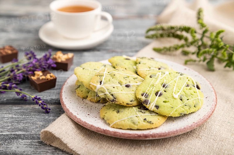 Green cookies with chocolate and mint on ceramic plate with cup of green tea and linen textile on gray wooden background. side view, close up, selective focus