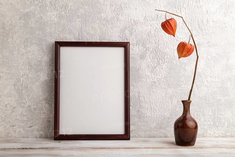 Brown wooden frame mockup with physalis in ceramic vase on gray concrete background. Blank, vertical orientation, still life, copy space
