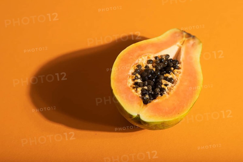 Ripe cut papaya on orange pastel background. Side view, close up, hard light. Tropical, healthy food, women health concept, minimalism