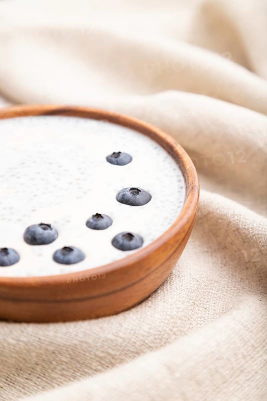 Yogurt with blueberry in wooden bowl on white wooden background and linen textile. Side view, close up, selective focus