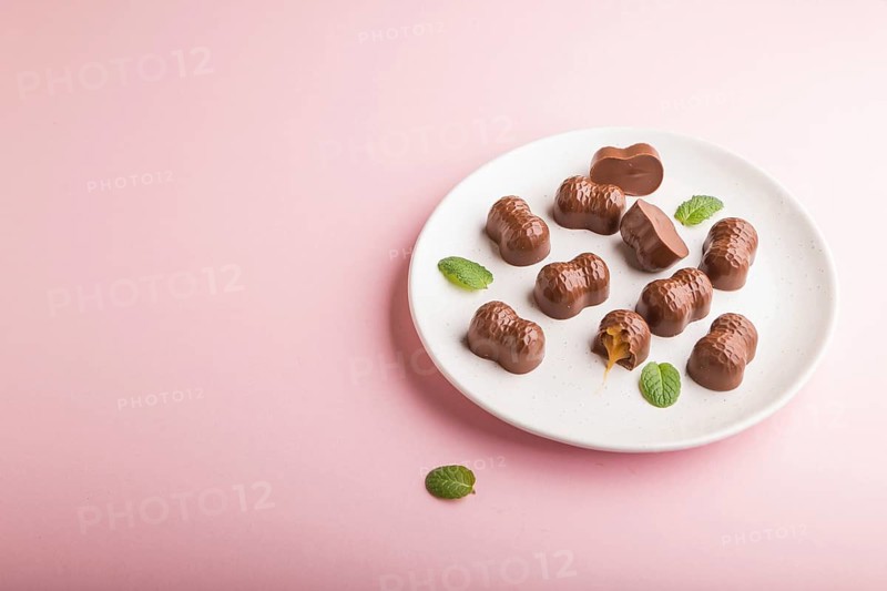 Chocolate caramel candies on a pastel pink background. Side view, copy space, close up
