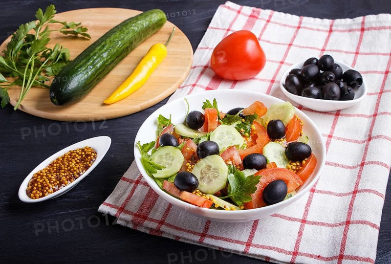 Vegetarian salad of tomatoes, cucumbers, parsley, olives and mustard on linen tablecloth and black wooden background, close up