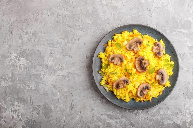 Yellow fried rice with champignons mushrooms, turmeric and oregano on blue ceramic plate on a gray concrete background. Top view, flat lay, copy space