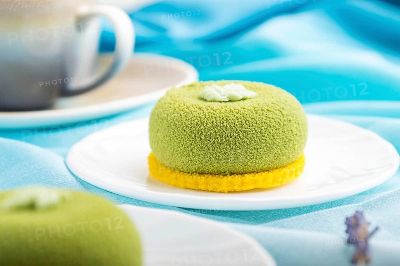 Green mousse cake with pistachio cream and a cup of coffee on a white wooden background and blue textile. side view, close up, selective focus