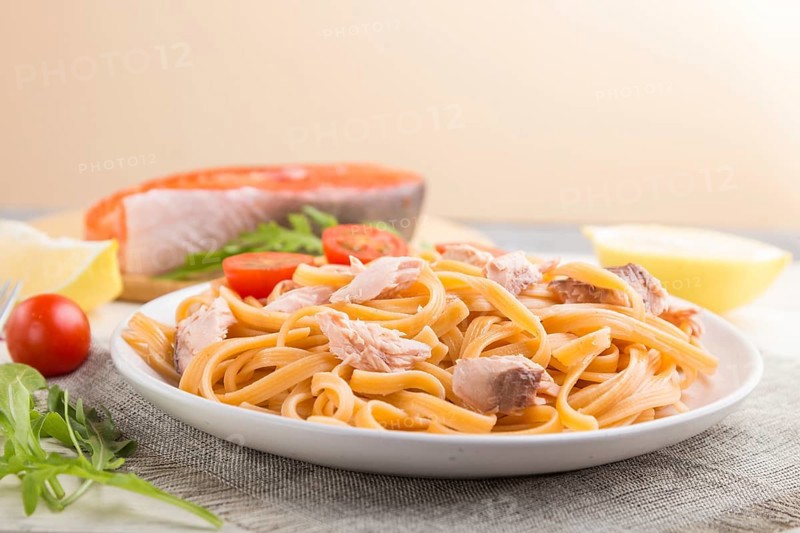 Semolina pasta with salmon and salmon steak on a white wooden background and linen textile. Side view, close up, selective focus