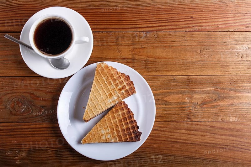 Waffle sandwiches with boiled condensed milk in plate on brown wooden table with cup of coffee. closeup, copy space, top view