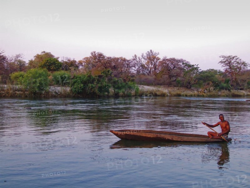 A Kavango fisherman pulls a net through a side arm of the Okavango River in the evening with his mokoro, a dugout canoe. Okavango, Divundu, Kavango West, Namibia, Africa