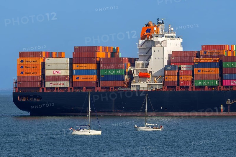 Sailboats sailing past stern of container ship, containership Hudson Express of the Hapag-Lloyd AG shipping company loaded with containers
