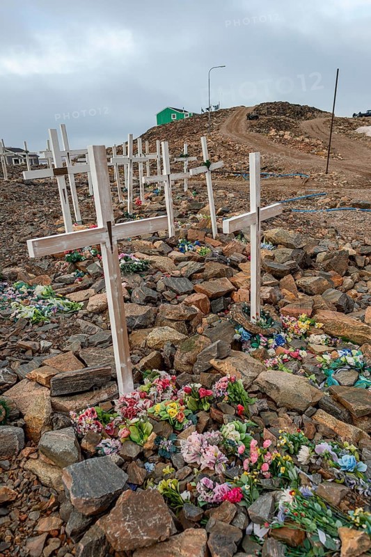 Row of graves with crosses and flowers on a stony cemetery under a grey sky, remote Arctic Inuit settlement Ittoqqortoormiit, Scoresbysund or Scoresby Sund or Greenlandic Kangertittivaq, East Greenland, Greenland, North America