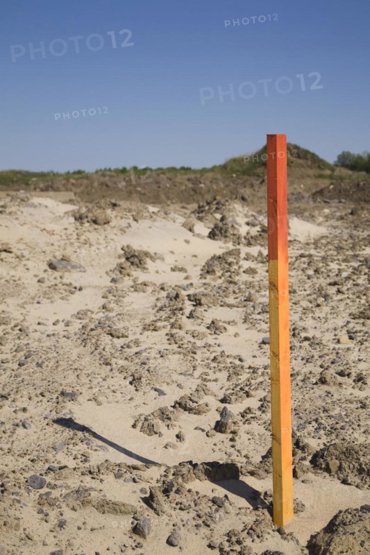 Red and orange painted wooden surveyor's stake or marker in sandy soil indicating a boundary line at construction site in spring, Quebec, Canada, North America
