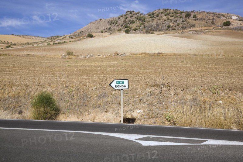 Black asphalt road and road sign in the middle of arid landscape indicating the direction to Ronda, Spain, Europe