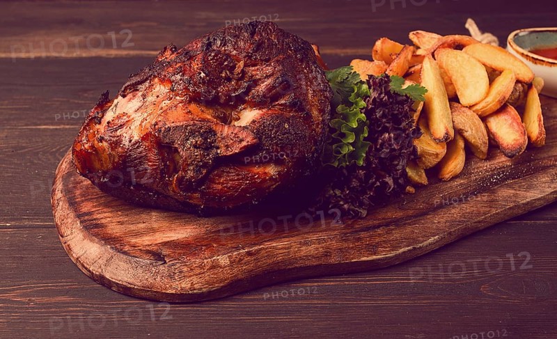 Pork knuckle, in soy-honey sauce, with fried potatoes, on a wooden chopping board, homemade, no people