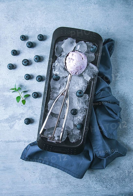 Blueberry ice cream, container with a spoon, on a gray table, fresh blueberries