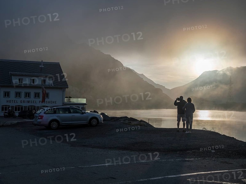 Sunrise on a foggy morning, hotel Grimsel mountain pass at lake Totensee, couple taking pictures, Switzerland, Europe