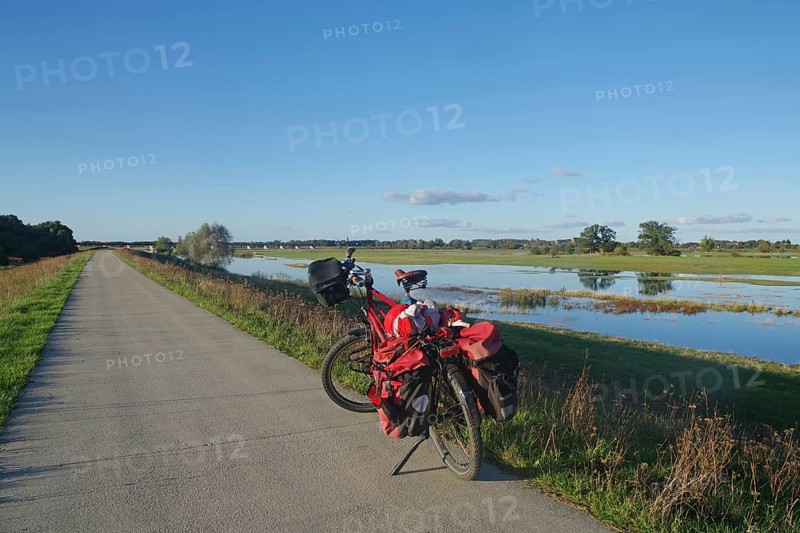 Red loaded bicycle on a road next to a wide landscape with water and sky, bicycle tourism, Langenfeld, Dömitz, Elbe, Wendland, Lower Saxony, Germany, Europe