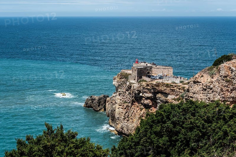 Lighthouse on the coast, on cliffs, surrounded by sea and forest, blue sky in the background, Fort São Miguel Acanjo, Farol de Nazaré, Lighthouse of Nazaré, Sítio, Sitio, Nazaré, Nazare, Oeste, District Leiria, Centro, Estremadura, Portugal, Europe