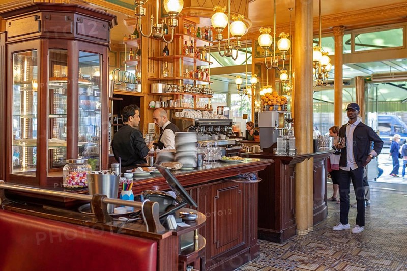 Elegant café with busy staff behind a glass-topped wooden counter, Paris