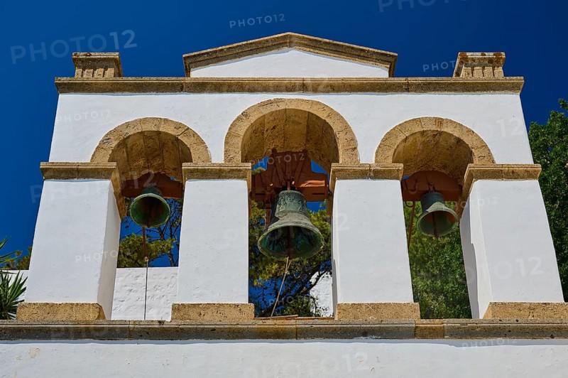 Cross-domed church of Diasososuan, white bell tower with three arches and hanging bells against a deep blue sky with ancient architectural details, Chora, Old Town, Patmos, Dodecanese, Greek Islands, Greece, Europe