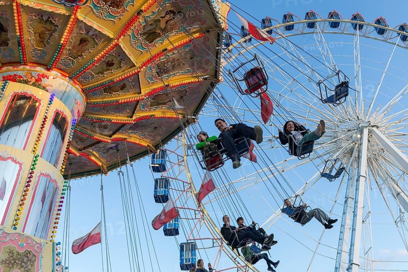 People swinging on a carousel in front of a Ferris wheel in sunny weather at a funfair, Europa Rad, Cannstadter Volksfest, Stuttgart-Bad Cannstadt, Baden-Württemberg