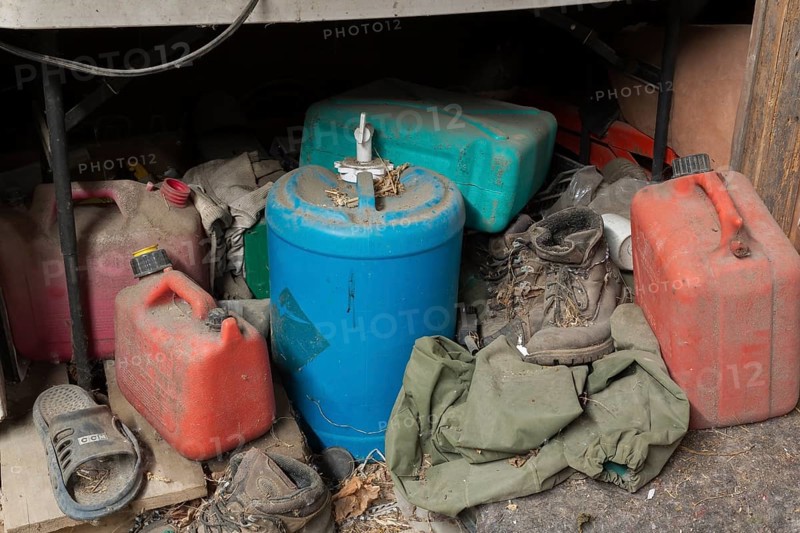 Old and dusty empty red plastic gas canisters, blue water containers and boots stored underneath a counter in an old barn, Quebec, Canada, North America