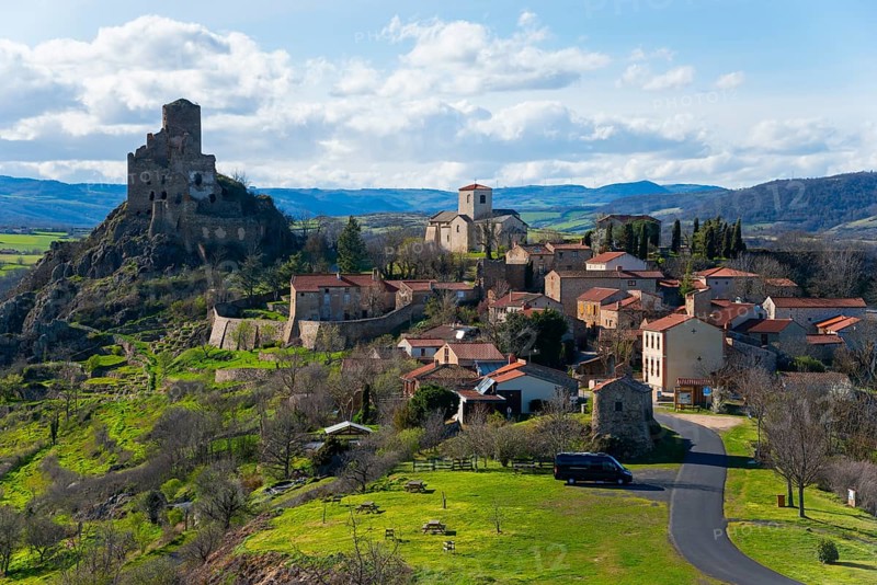 Ein malerisches Dorf mit einer alten Burgruine auf einem Hügel, umgeben von grüner Natur und blauem Himmel, Léotoing, Leotoing, Haute-Loire, Auvergne-Rhône-Alpes, Auvergne-Rhone-Alpes, Frankreich