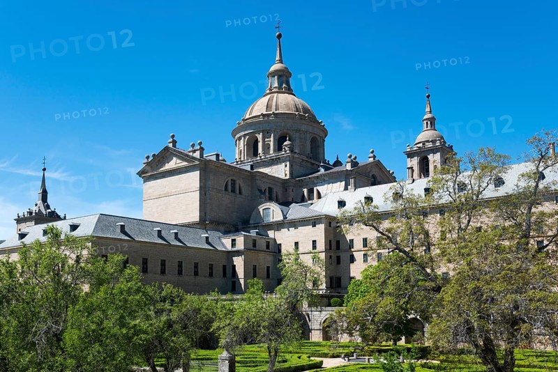 Impressive historic monastery with towers and domes surrounded by green trees under a blue sky, Real Sitio de San Lorenzo de El Escorial, Royal Seat of St Lawrence of El Escorial, palace and monastery complex, San Lorenzo de El Escorial, Madrid, Spain, UNESCO World Heritage Site, Europe