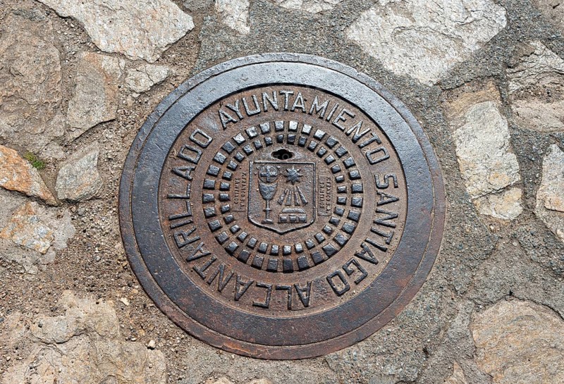 A round metal manhole cover with a coat of arms and text on a paved surface, manhole cover, gully cover, Santiago de Compostela, autonomous community of Galicia, place of pilgrimage, destination of the Way of St James, Spain, Europe
