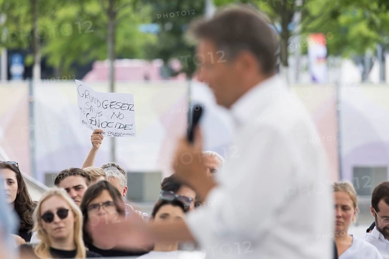 A visitor with a Palestinian scarf holds a piece of paper with the inscription Grundgesetzt Says No Genocide at the dialogue format with Robert Habeck (Vice Chancellor and Federal Minister for Economic Affairs and Climate Protection, The Greens) on the topic: What it's all about: Protecting freedom and democracy, renewing prosperity in the dialogue forum at Demokratie feiern. / The Basic Law turns 75, together it will be a celebration, Berlin, 25.05.2024