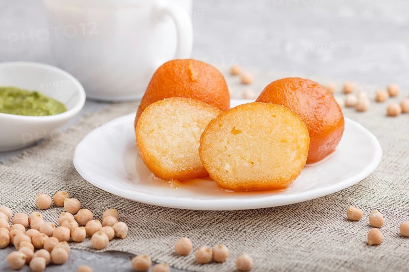 Traditional indian candy gulab jamun in white plate with mint chutney on a gray concrete background. side view, close up