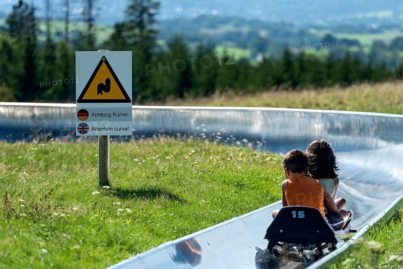 Boy and girl with sledges on the summer toboggan run, warning sign Attention curve, ski and toboggan arena, summit mountain Hoherodskopf, excursion destination, Schotten, Vogelsberg Volcano Region nature park Park, Hesse, Germany, Europe