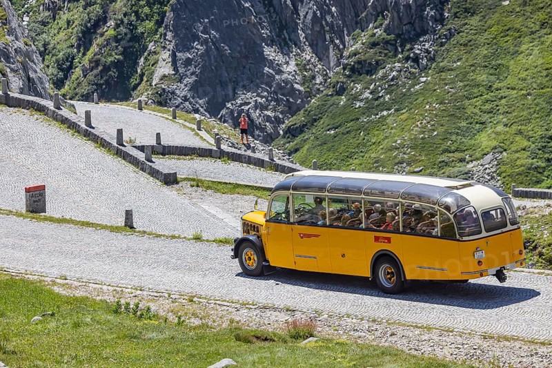 Historic postbus travelling along the Tremola, the world-famous serpentine road through the Val Tremolo. Tourist bus on the Tremola road, Switzerland's longest road construction monument with 24 hairpin bends. Airolo, Canton Ticino, Switzerland, Europe