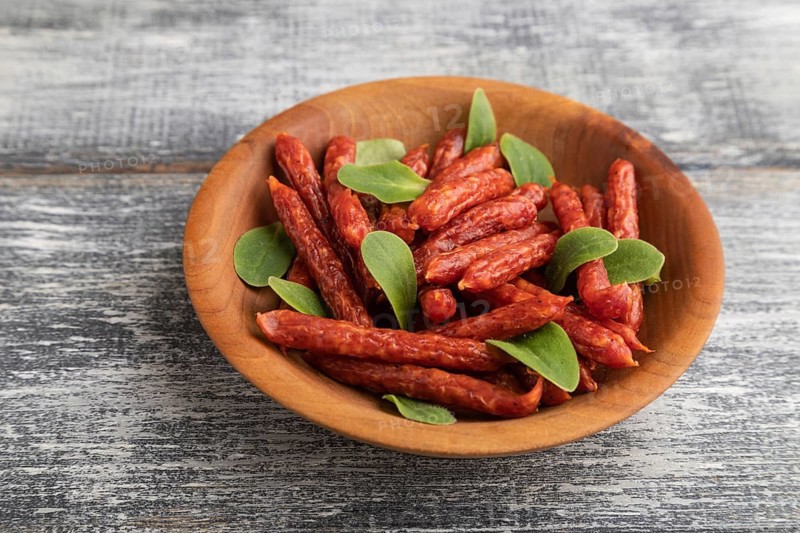 Small smoked sausage with borage microgreen, salt and pepper on gray wooden background. Side view, close up